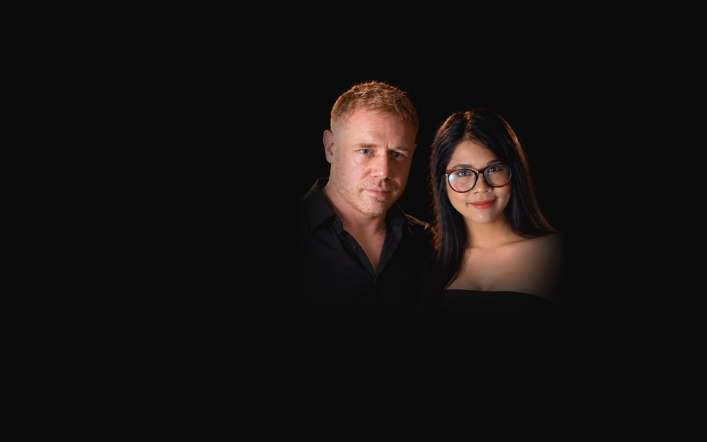 Tim and Paemi side by side in black against a black background, facing the camera